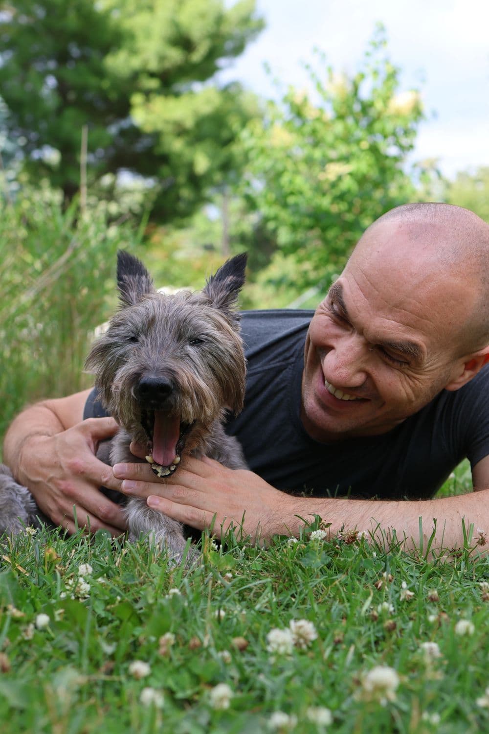 A man lying in the grass laughing with his cairn terrier